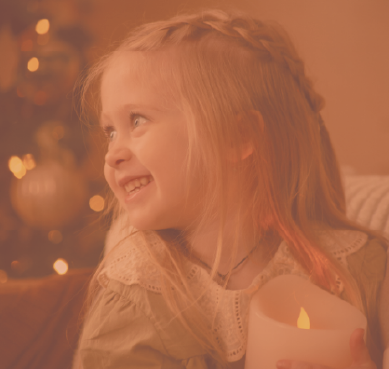 Une petite fille tenant une bougie et elle sourit, elle est heureuse