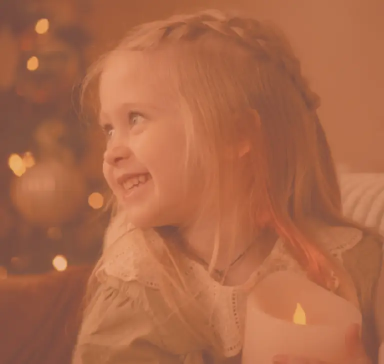 Une petite fille tenant une bougie et elle sourit, elle est heureuse