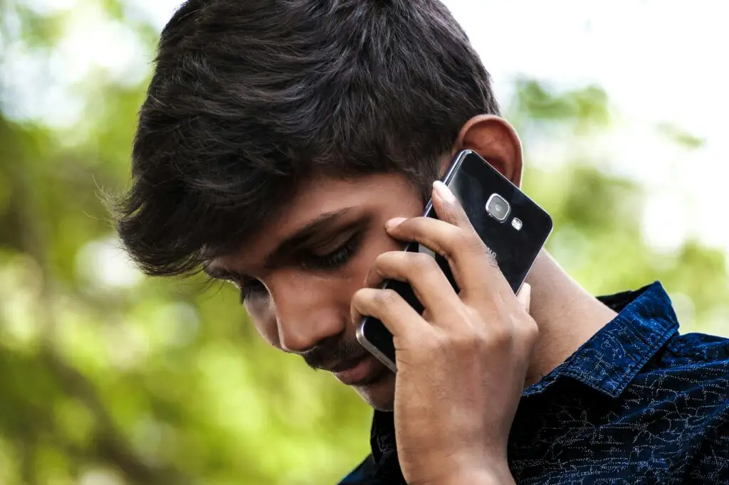 Jeune hommes tenant son téléphone dans sa main proche de son oreille.